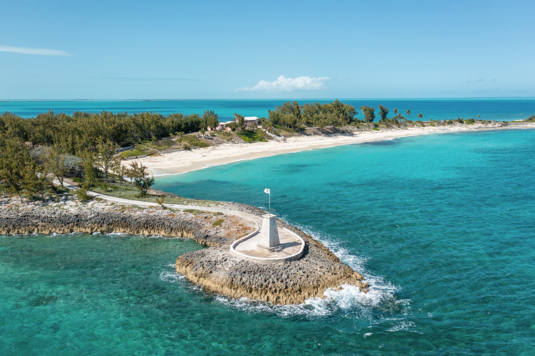 Aerial view of a private Bahamas island at golden hour with a stone lighthouse and turquoise water